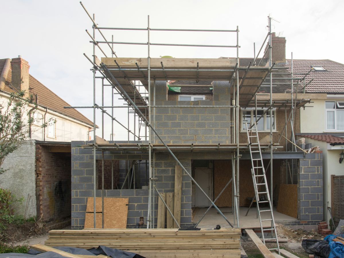 Aanbouw in betonblokken met stelling achter een rijwoning
